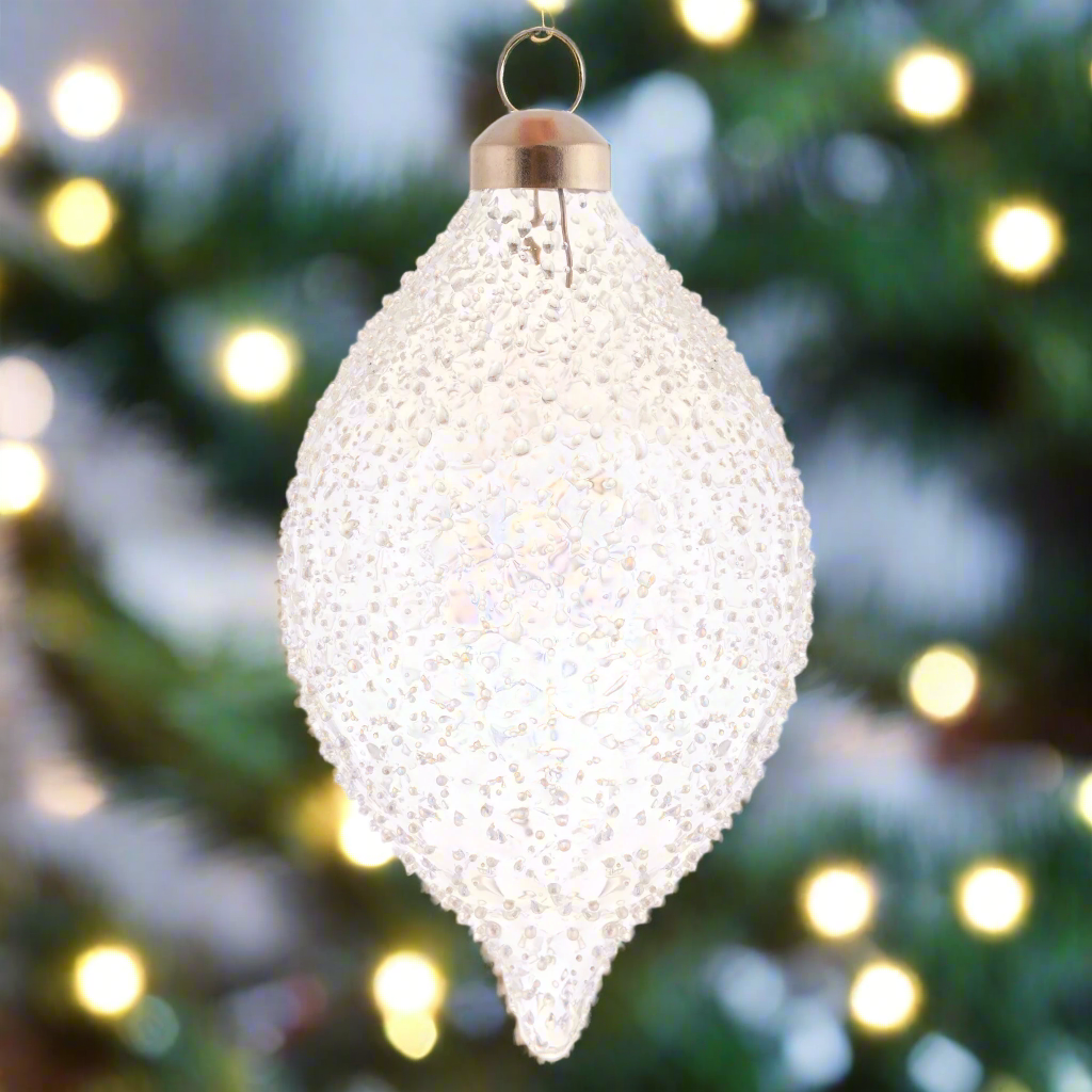 Icy Snow Glass Ornaments with holiday lighting in the background.