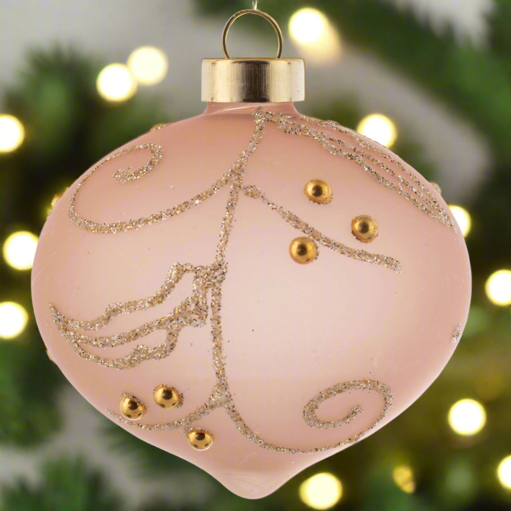 Gold Glitter Leaf Glass Ornament Blush with holiday lighting in the background.