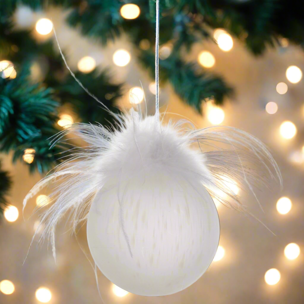 Speckled Feather Top Glass Frosted Ornament with holiday lighting in the background.