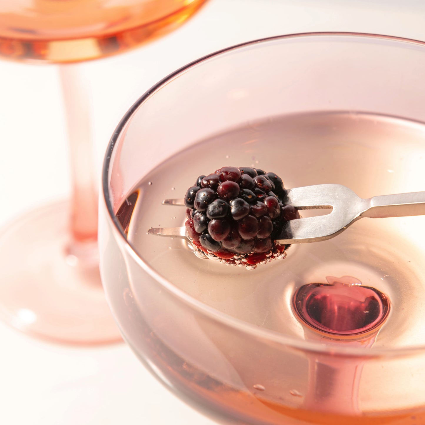 Blush Mid Century Champagne Coupes close up view, cocktail with a blackberry.