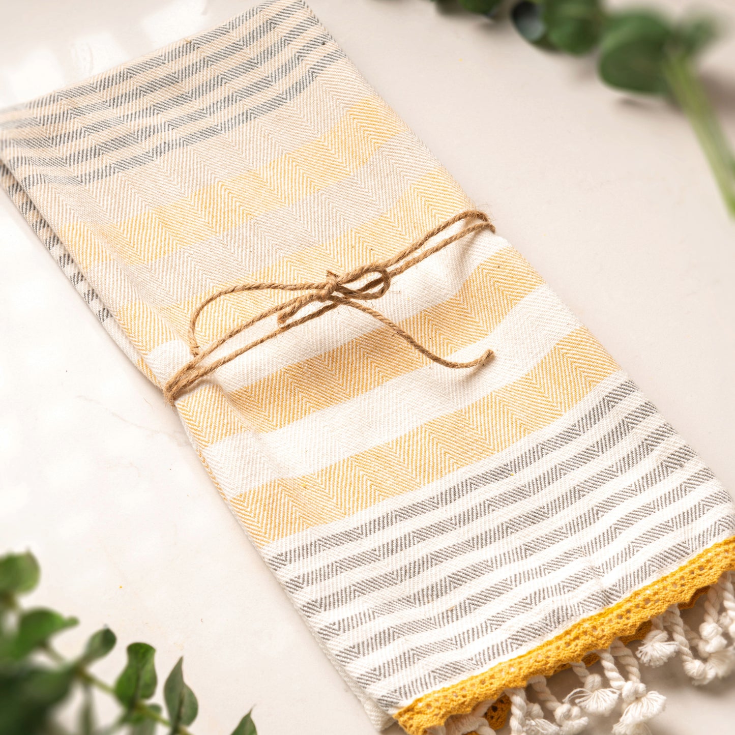 Mustard/Gray Studio Tea Towel on a table with foliage accents.