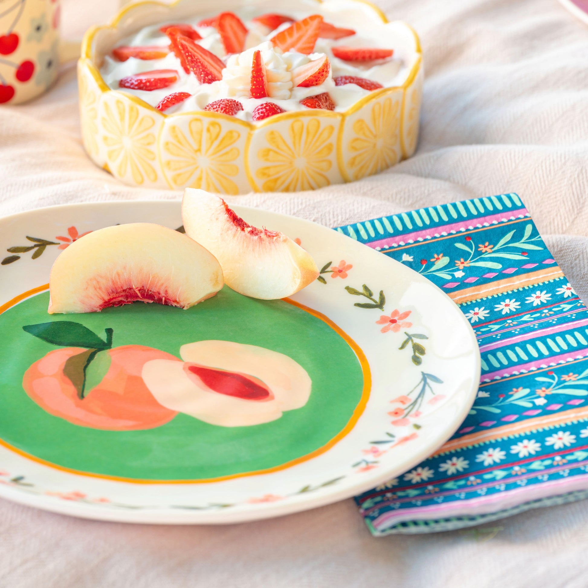 Peaches Melamine Salad Plates on a white cloth with peaches on the plate, lemon dish with strawberries and cream in background.