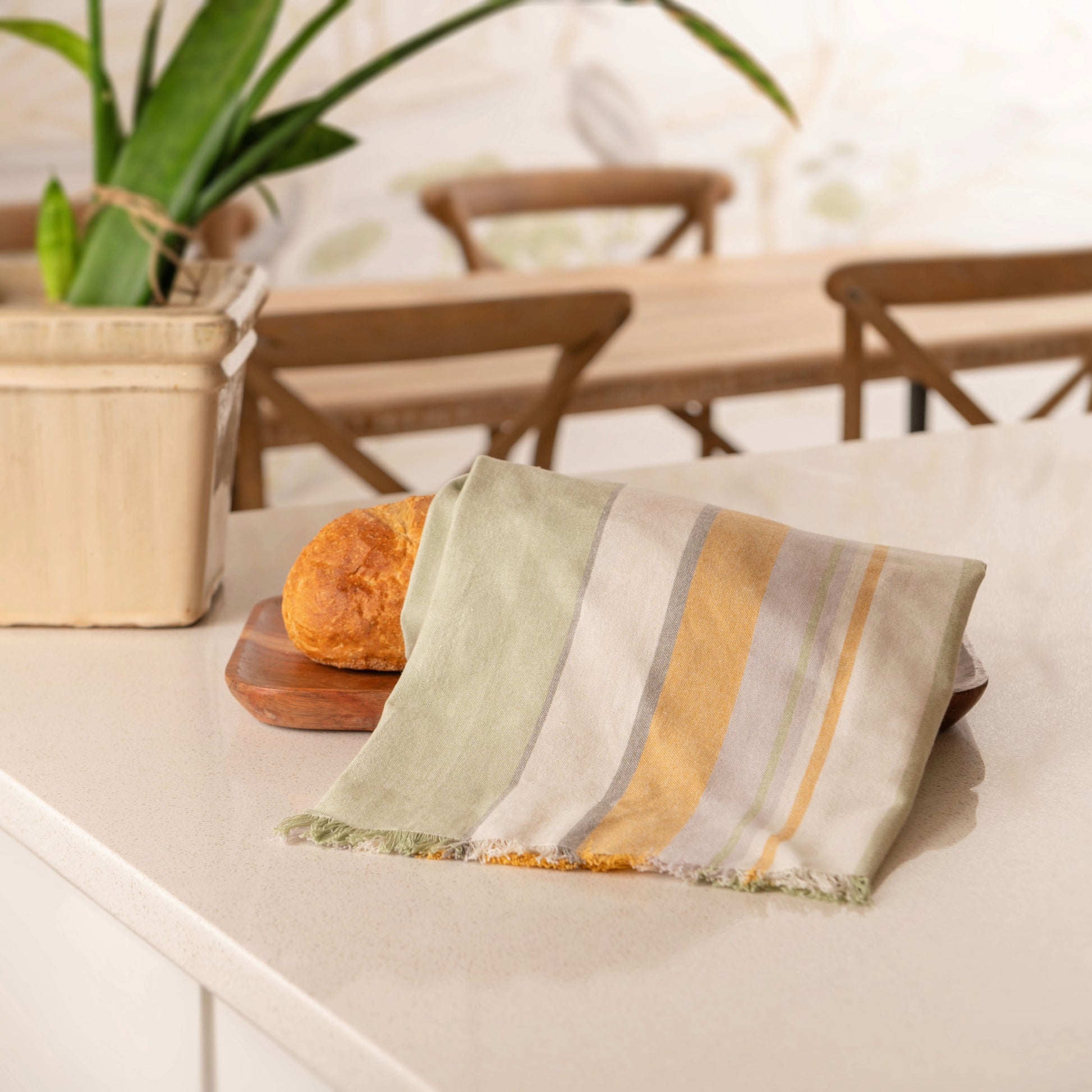 Green/Mustard Waterfront Tea Towel on a loaf on bread, on a kitchen counter.