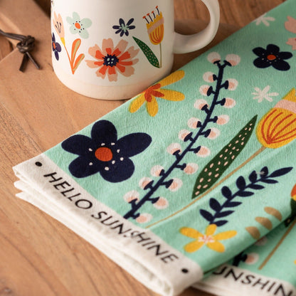 More Happy Shelly Tea Towel on a table with a mug. 