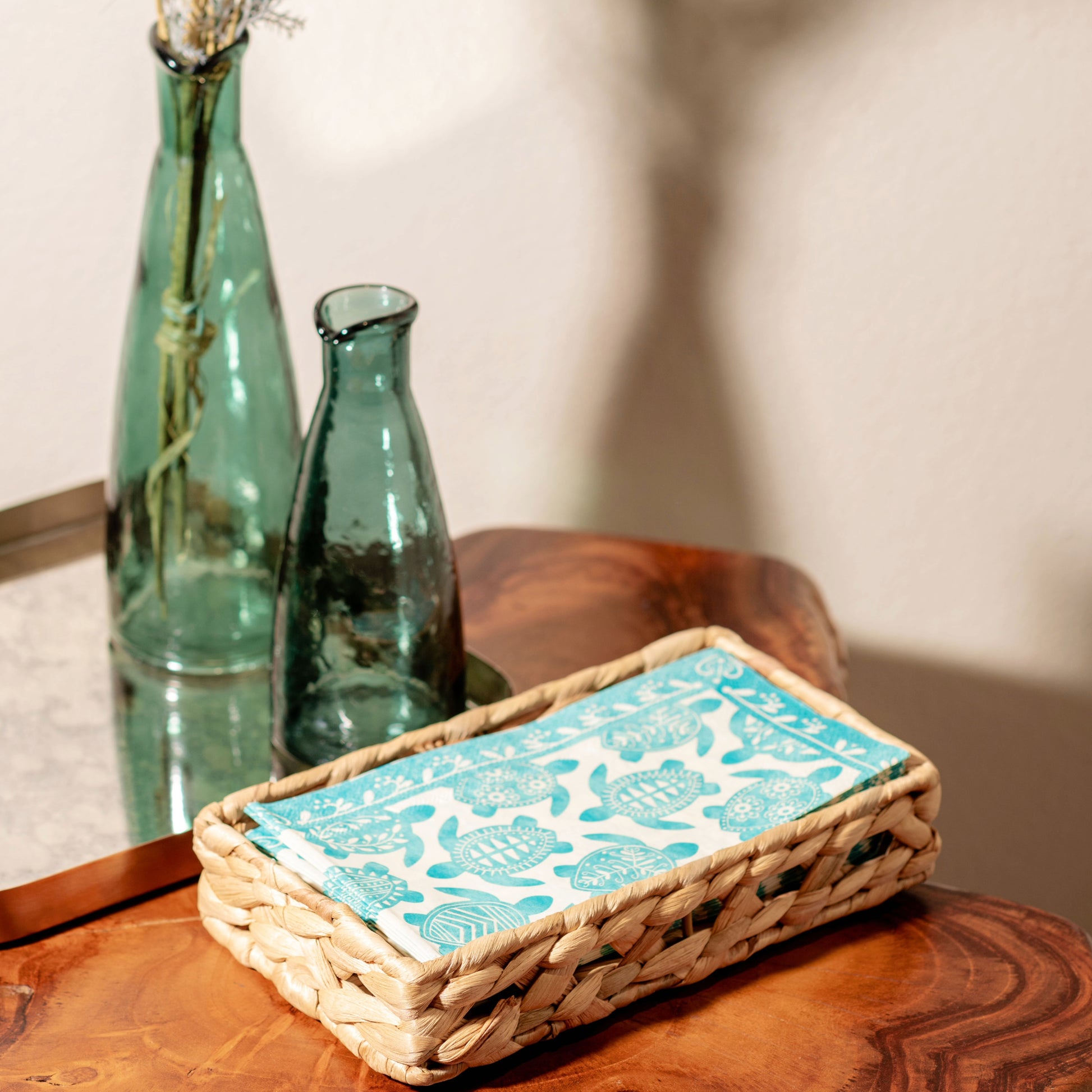 Turtle Woven Napkin Holder w/ Paper Napkins on a table with carafes in background. 