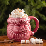 Pink santa mug on a table with whipped cream and marshmallows.